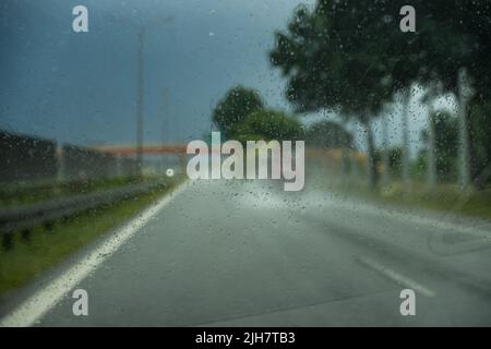 Conduite de la voiture sur l'autoroute en cas de forte pluie. Vue de la vitre avant vers la route. Pare-brise plein de gouttes de pluie floues. Banque D'Images