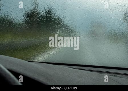 Conduite de la voiture sur l'autoroute en cas de forte pluie. Vue de la vitre avant vers la route. Pare-brise plein de gouttes de pluie floues. Banque D'Images