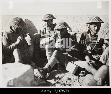 Une photo vintage vers 1942 montrant le second lieutenant Charles Hazlitt Upham et les soldats de la division de Nouvelle-Zélande dans le désert occidental manger des rations sur le terrain. Au centre se trouve le second lieutenant Charles Hazlitt Upham, qui a reçu le V.C. et le bar pour ses combats en Crète et en El Alamein en Afrique du Nord pendant la deuxième guerre mondiale. Il était l'une des trois personnes à recevoir deux fois la Croix de Victoria Banque D'Images