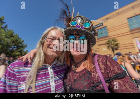 Southend on Sea, Royaume-Uni. 16 juillet 2022. Deux individus posent ensemble lors d'un événement en plein air dynamique à Brighton. L'un porte un polo à rayures violettes, tandis que l'autre porte un chapeau à plumes avec des lunettes, des lunettes de soleil réfléchissantes et un haut à motifs noir et rouge. Les 1000 participants se réunissent pour l'événement Southend Pride, avant que le défilé ne commence le long de High Street et dans les jardins de Warrior Square pour un festival de la fierté avec des spectacles d'animation. Penelope Barritt/Alamy Live News Banque D'Images