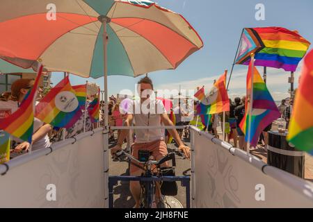 Southend on Sea, Royaume-Uni. 16 juillet 2022. Un participant pédalera un flotteur de vélo stationnaire sous un parapluie arc-en-ciel lors d'un défilé Pride au Royaume-Uni. La scène est vibrante avec des drapeaux arc-en-ciel, des tenues festives et des célébrations communautaires sous un ciel clair d'été. Les 1000 participants se réunissent pour l'événement Southend Pride, avant que le défilé ne commence le long de High Street et dans les jardins de Warrior Square pour un festival de la fierté avec des spectacles d'animation. Penelope Barritt/Alamy Live News Banque D'Images