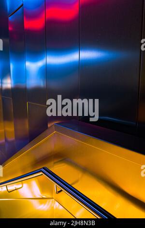 Un plan vertical d'un couloir moderne avec rambarde d'escalier et murs métalliques illuminés de lumières colorées Banque D'Images