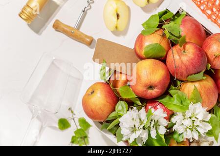 Pommes de ferme, bouteille de cidre, verre et tire-bouchon sur fond blanc. Composition écologique avec Summer, Low-Alcohol, boisson aux fruits. Fruits W Banque D'Images