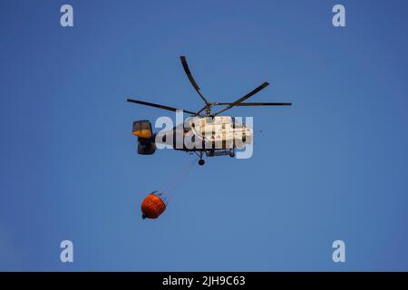 Hélicoptère lourd de l'INFOCA transportant un seau d'eau pour se déposer sur un feu de forêt, Mijas, Espagne. Banque D'Images