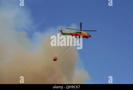 Hélicoptère de taille moyenne de l'INFOCA transportant un seau d'eau pour tomber sur un feu de forêt, Mijas, Espagne. Banque D'Images