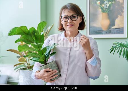 Femme d'âge moyen souriante avec plante en pot à la maison Banque D'Images
