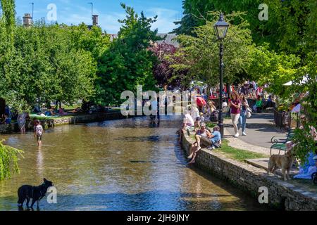 Foules au bord de la rivière Windrush à Bourton sur l'eau lors d'une chaude journée d'été, Gloucestershire, Angleterre. Banque D'Images