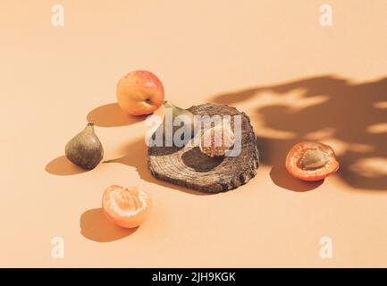 Composition de style vintage composée de figues sur podium en bois, abricots et ombre d'arbre sur fond orange. Concept alimentaire de style rétro. Banque D'Images