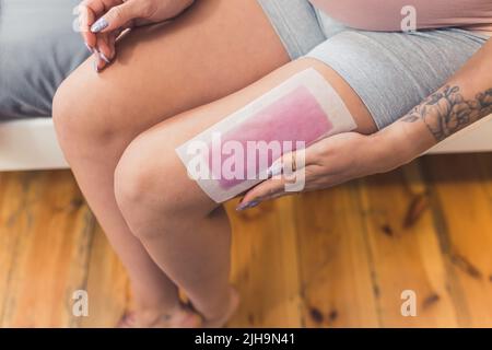 femme effectuant une procédure d'épilation des jambes avec des bandelettes cirées, en intérieur, en gros plan. Photo de haute qualité Banque D'Images