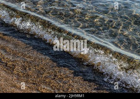 Vagues de mer se brisant sur la plage avec du sable et des cailloux Banque D'Images