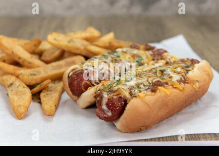 Paire de hot dogs au fromage Chili chargés de fromage fondu et servis avec des frites au steak de poivre pour un repas de faim d'appétit de fête. Banque D'Images