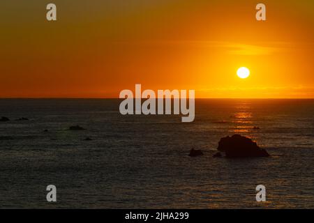 Lever de soleil doré sur un horizon lointain et rochers hors-rivage dans la baie de Kaikoura. Banque D'Images