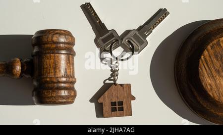 Des clés avec porte-clés en forme de maison et un gavel de juge sur fond blanc. Banque D'Images