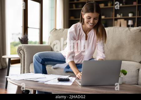 Une femme souriante paie ses factures, gère ses finances et utilise son ordinateur portable à la maison Banque D'Images