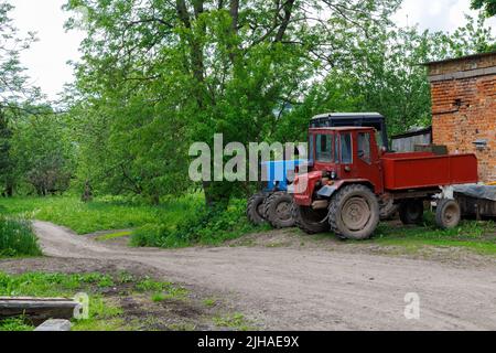 deux vieux tracteurs soviétiques près d'un bâtiment en briques dans un jardin de pommes de jour d'été Banque D'Images