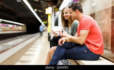 Le couple attend le train sur le banc et regarde sur la carte Banque D'Images