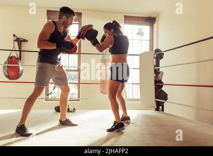 Boxer jeune femme pratiquant des combinaisons de poinçonnage avec son entraîneur personnel. Jeune femme sportive ayant une séance d'entraînement dans un gymnase de boxe. Banque D'Images