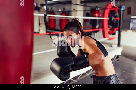 Une femme qui s'est fait duquer après avoir percuter un sac de poinçonnage dans une salle de fitness. Boxeur jeune femme ayant une session d'entraînement à côté d'un anneau de boxe. Banque D'Images