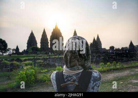 Vue de l'arrière de la jeune femme musulmane asiatique portant le hijab regardant le temple pendant le coucher du soleil à l'ancien temple de Prambanan en Indonésie. Banque D'Images