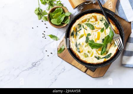 Omelette aux épinards et au fromage. Frittata fait d'oeufs, de paprika et d'épinards dans une poêle sur un comptoir en marbre. Vue de dessus. Copier l'espace. Banque D'Images