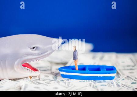 Homme miniature sur un petit bateau bleu face à un requin prêt sur l'océan dollar. Concept de requin de prêt. Banque D'Images