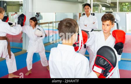 Deux garçons en gants de boxe lançant des coups pendant l'entraînement d'auto-défense dans la salle de gym Banque D'Images