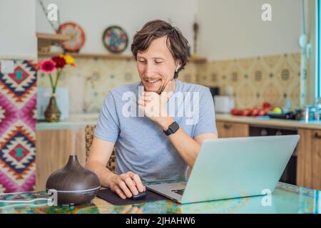 Diffuseur d'huile essentiel sur la table en cours de cuisson pendant que l'homme utilise un ordinateur portable Banque D'Images
