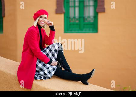 Femme heureuse élégante assise à la frontière près d'un bâtiment de couleur vieilli Banque D'Images