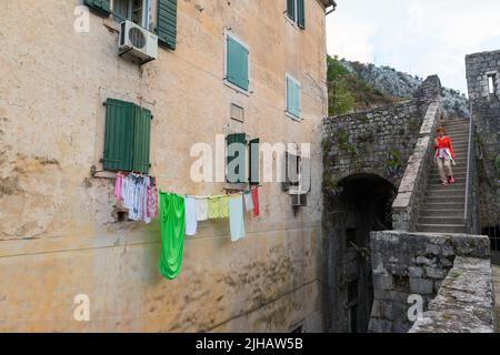 Une touriste féminine en vêtement orange descend un escalier historique près d'une vieille maison avec une ligne de lavage dans la vieille partie de Kotor, au Monténégro Banque D'Images