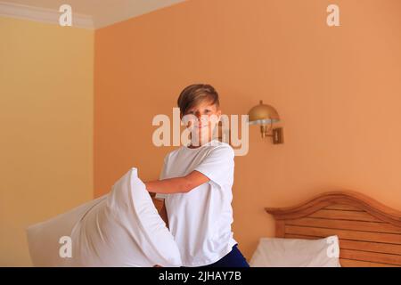 Combat d'oreillers. Un enfant avec un oreiller dans les mains. Un garçon se trouve sur un lit avec des draps blancs dans une chambre d'hôtel. L'enfant dort. Adolescent au lit à la maison Banque D'Images