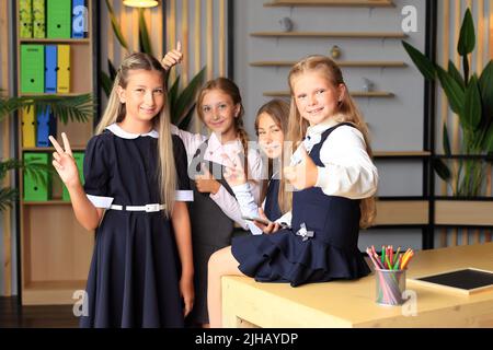 Jeunes élèves de sexe féminin en uniforme scolaire avant la leçon en classe. Enseignement à distance. La compagnie de filles d'école dans la classe. École primaire Banque D'Images