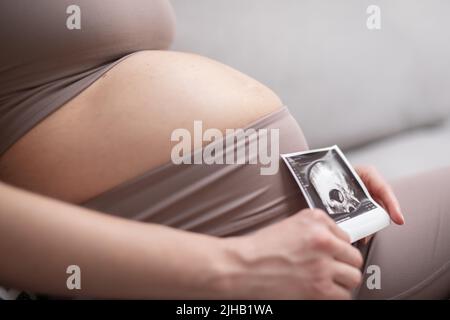 Femme enceinte ventre. Concept de grossesse. Ventre de la femme enceinte en gros plan. Détail de la femme enceinte se relaxant sur un canapé confortable à la maison. Banque D'Images