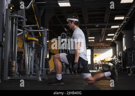 Profil plein plan d'un fitnessman faisant des fentes avec des haltères Banque D'Images