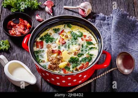 Zuppa Toscana, soupe toscane copieuse, accompagnée de saucisses italiennes, de kale, de bacon et de pommes de terre dans une marmite rouge sur une table en bois sombre Banque D'Images