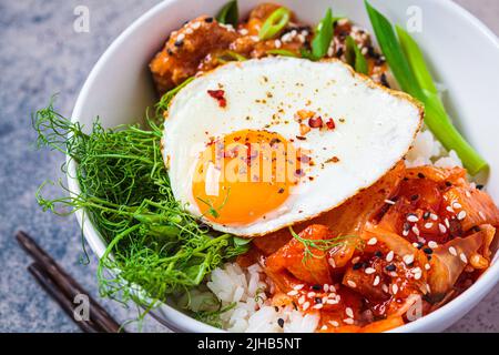 Bibimbap - viande, riz, kimchi, œuf et pousses dans un bol blanc. Cuisine traditionnelle coréenne. Banque D'Images