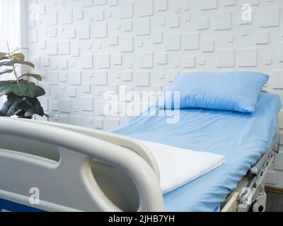Vider le lit du patient dans une chambre d'hôpital avec un coussin bleu et une drap de lit sur fond blanc. Lit de maladie dans la salle de récupération avec dosreet réglable électrique Banque D'Images
