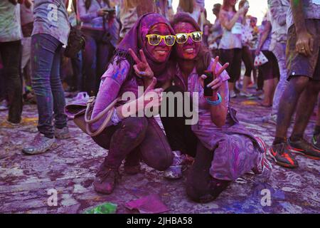 Deux femmes couvertes de poudre colorée posent pour une photo sur le terrain à la Color Walk à Dubaï, Émirats arabes Unis. Les deux sourient avec des nuances jaunes. On a un hijab. Banque D'Images