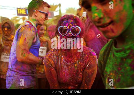 Une jeune femme aux teintes en forme de cœur sourit pour une photo au milieu d'une foule également couverte de poudre colorée à la Color Walk à Dubaï, aux Émirats arabes Unis. Banque D'Images