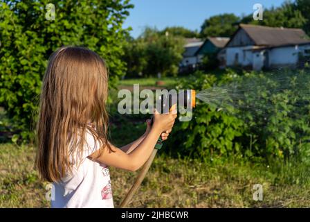 Une petite fille utilise un jet d'eau pour arroser les arbres dans le jardin Banque D'Images