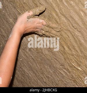 Main d'une jeune femme qui construit un mur écologique avec de l'argile et du plâtre de paille. Construction en matériaux naturels Banque D'Images