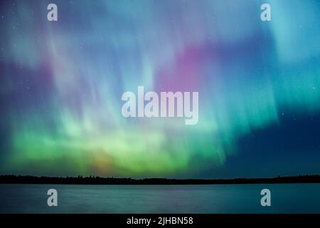 Les aurores boréaux éclatent au-dessus d'un lac du Minnesota dans le ciel sombre qui illumine un arc-en-ciel de lumière et de couleurs Banque D'Images