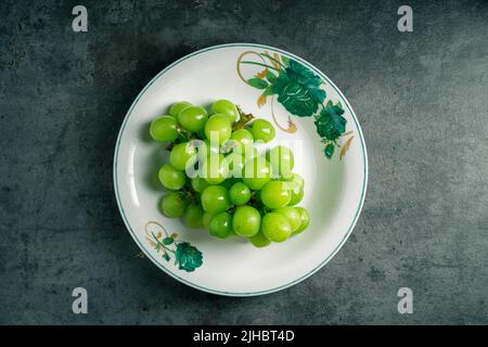 Bol de raisins verts isolé sur fond gris. Vue de dessus. Prise de vue dans l'obscurité. Lieu d'écriture. Banque D'Images