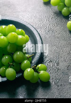 Une branche de raisins verts juteux dans une assiette. Arrière-plan noir. Vue avant. Lieu d'écriture. Idéal pour l'été. Banque D'Images