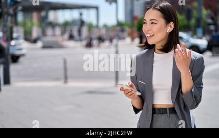 Jeune femme asiatique parlant au téléphone avec des écouteurs sans fil dans la rue de la ville. Banque D'Images