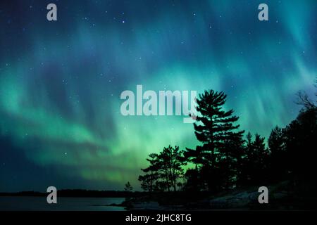 Les aurores boréaux éclatent au-dessus d'un lac du Minnesota dans le ciel sombre qui illumine un arc-en-ciel de lumière et de couleurs Banque D'Images