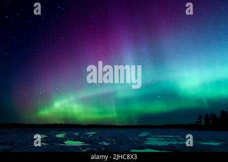 Les aurores boréaux éclatent au-dessus d'un lac du Minnesota dans le ciel sombre qui illumine un arc-en-ciel de lumière et de couleurs Banque D'Images