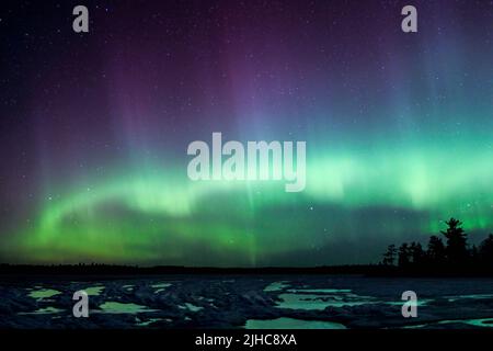 Les aurores boréaux éclatent au-dessus d'un lac du Minnesota dans le ciel sombre qui illumine un arc-en-ciel de lumière et de couleurs Banque D'Images