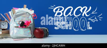 Sac à dos avec papeterie, horloge et pomme sur table sur fond bleu. Retour à l'école Banque D'Images