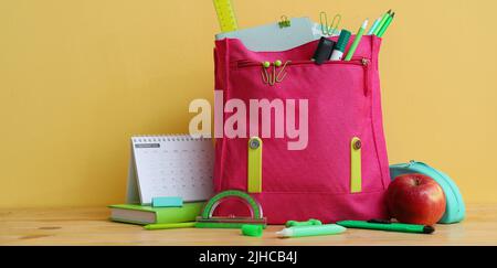 Sac à dos d'école avec papeterie et pomme sur table sur fond de couleur Banque D'Images