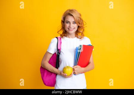 Portrait d'une femme heureuse tenant un sac à dos. Processus d'étude. Jeune fille étudiante mignonne avec sac à dos contient quelques documents et des livres sur fond jaune. Banque D'Images